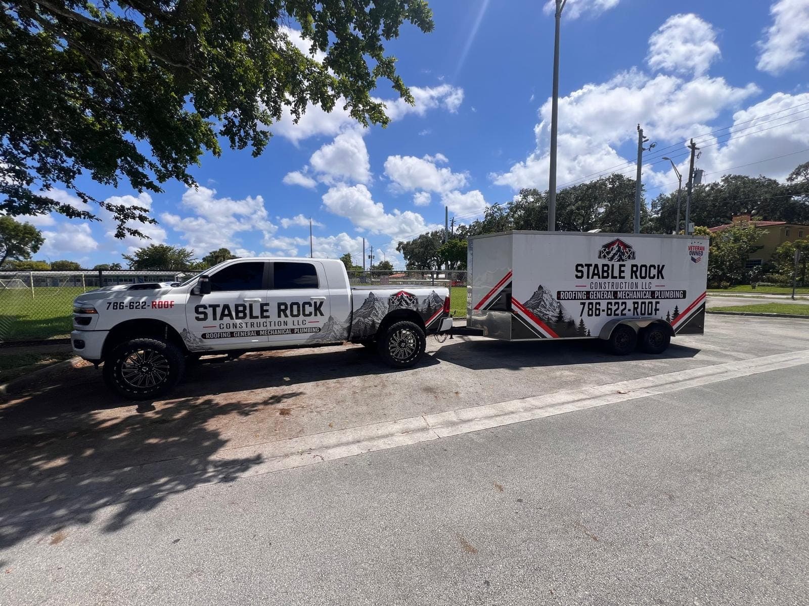 Stable Rock Construction’s white wrapped Ram pickup towing a matching enclosed trailer with a Veteran Owned badge, under a clear blue sky.